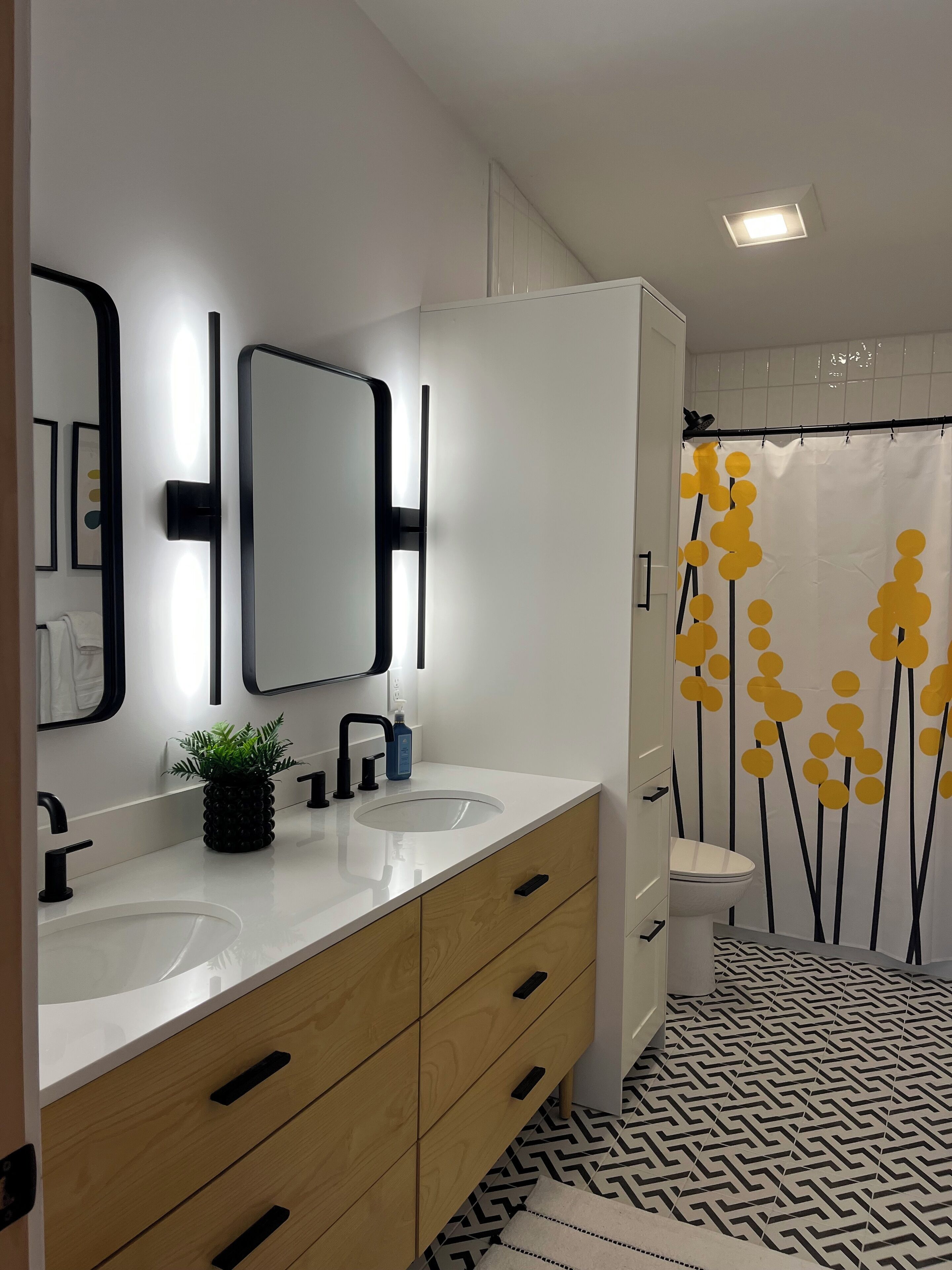 Ein modernes Badezimmer mit zwei Waschbecken, einem Spiegel, einer Topfpflanze und einem Duschvorhang mit gelbem Blumenmuster.