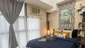 A bedroom with a bed, curtains, a wall-mounted artwork, a bedside table, and a bedside lamp.
