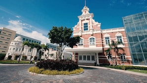A historic building with a prominent tower, surrounded by modern structures and a landscaped garden.