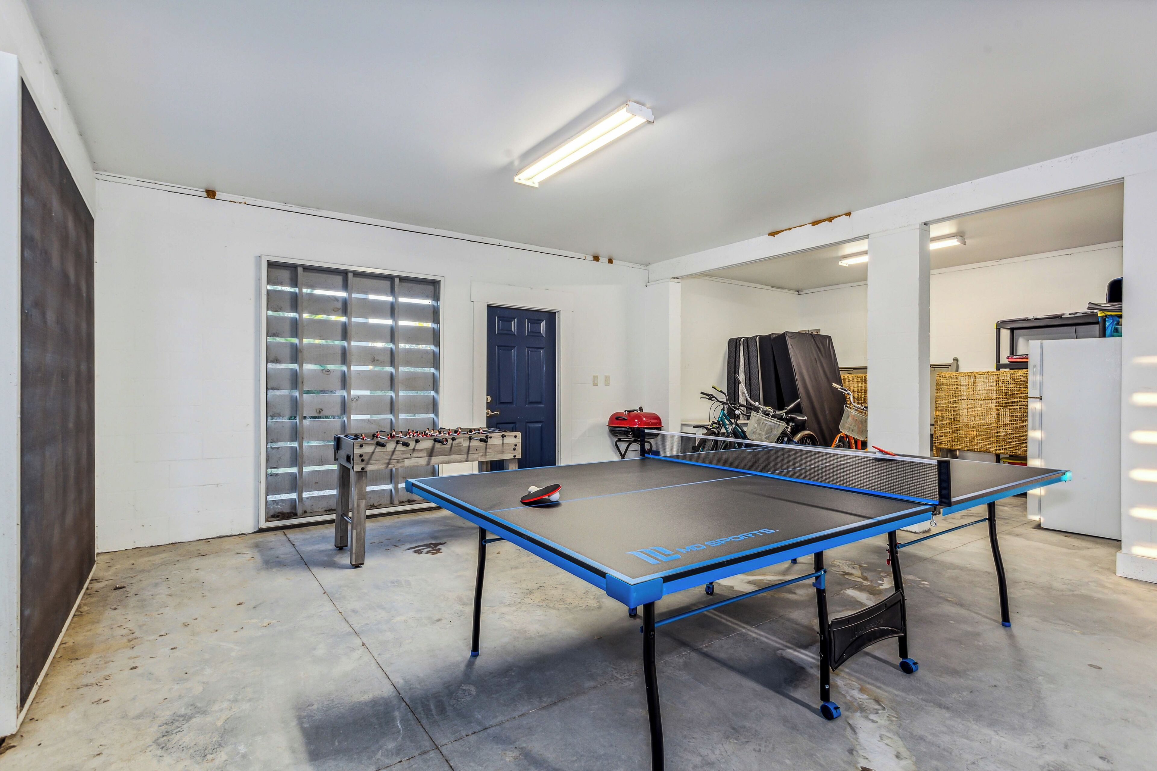 A ping pong table in a room with a door, a window, and a bicycle in the background.