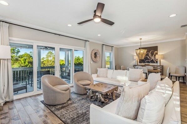A spacious living room with a large sofa, two armchairs, a coffee table, and a dining area with a chandelier.