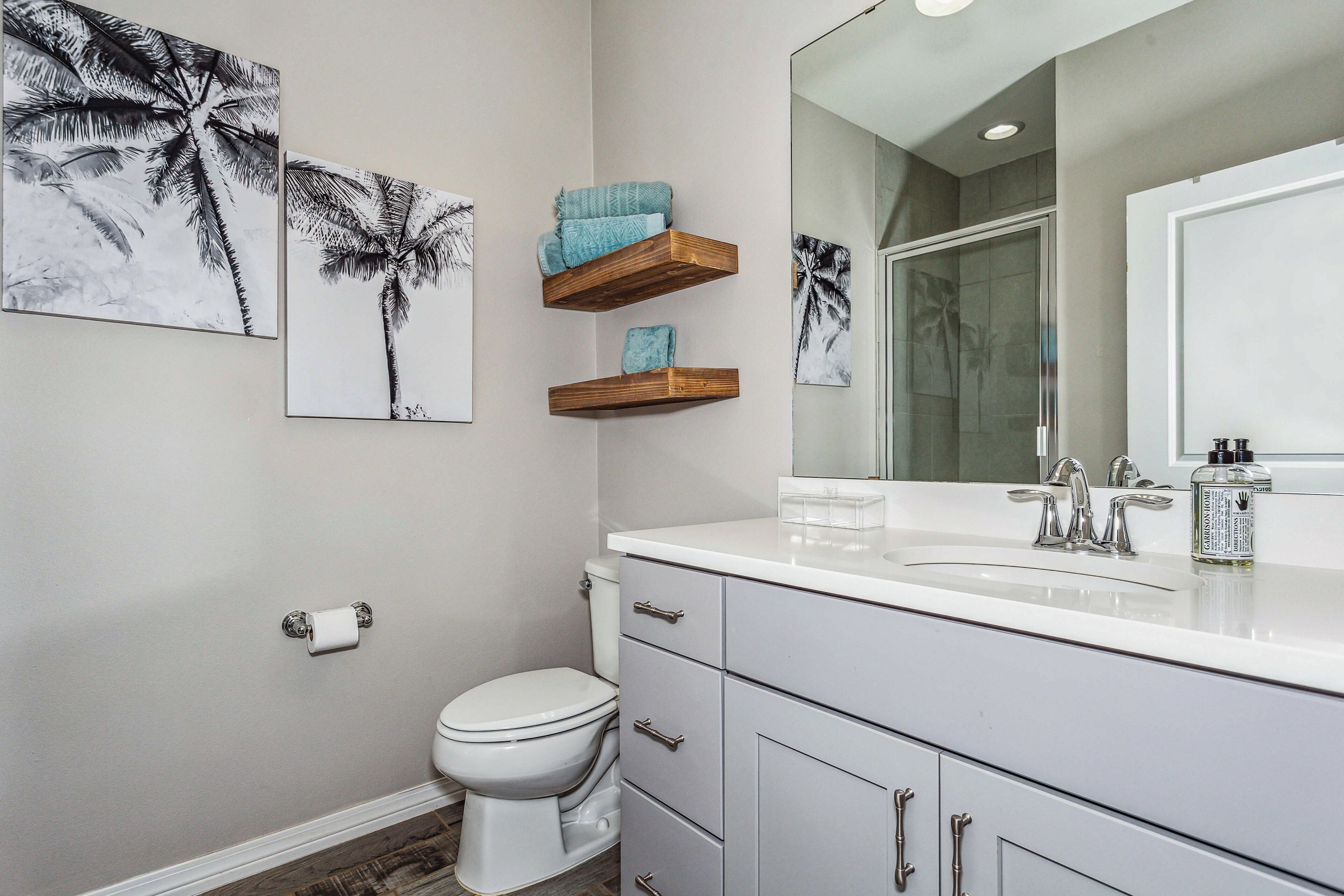 A bathroom with a toilet, a sink with a mirror, and two wall-mounted shelves with towels.