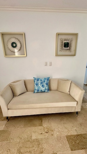 A beige sofa with a blue patterned pillow, two framed abstract wall art pieces, and a marble floor. - Luxury Golf Villa in Exclusive Punta Cana Resort (Punta Cana)
