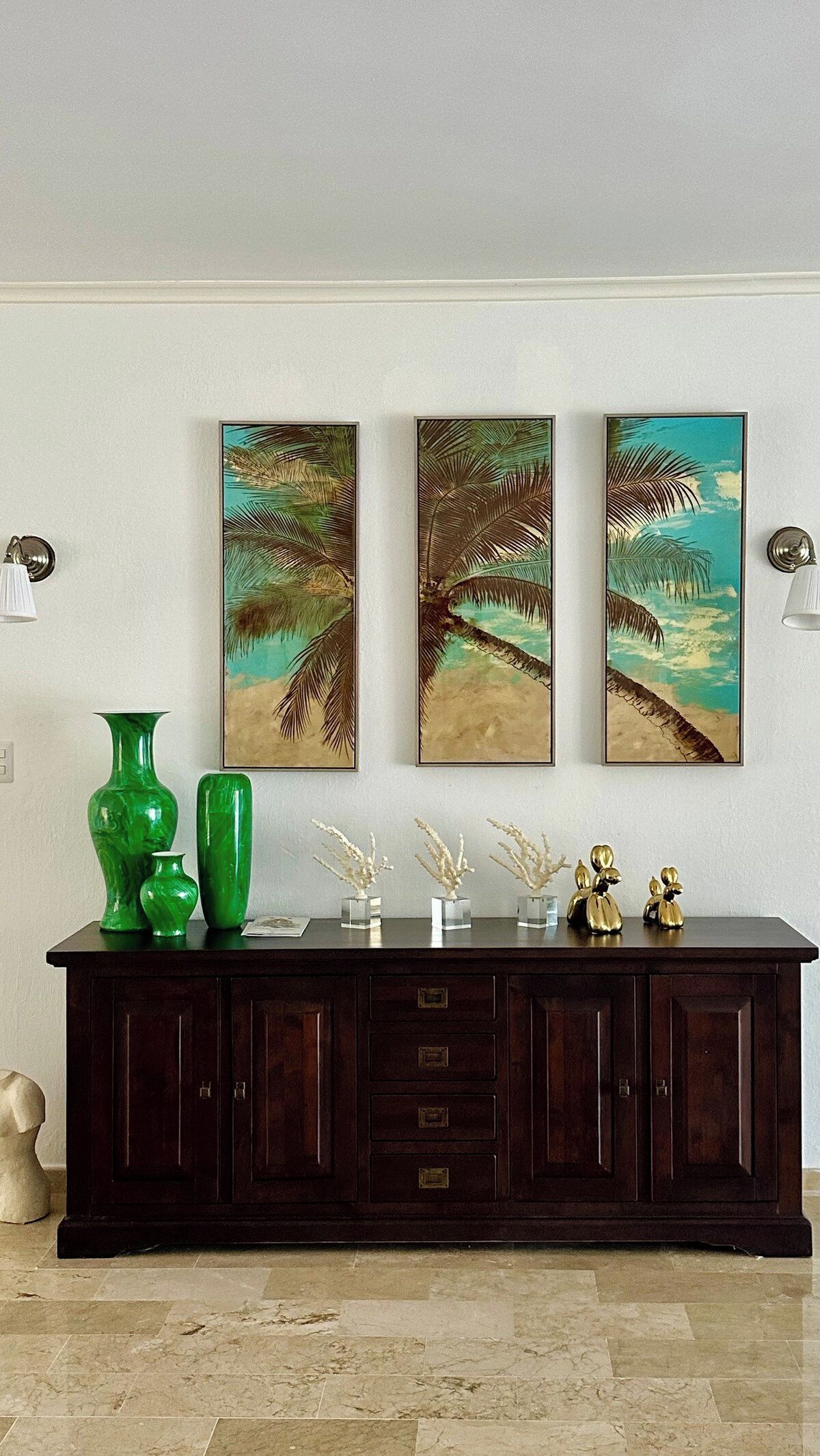 A dark wooden console table with three framed artworks above it, a green vase, and a decorative item on the table.