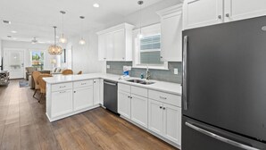 Une cuisine moderne avec des meubles blancs, un réfrigérateur noir et un coin repas doté de chaises en osier.