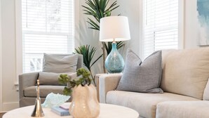 Un salon avec un canapé beige, une table basse ronde agrémentée d’objets décoratifs, une lampe bleue et une plante.