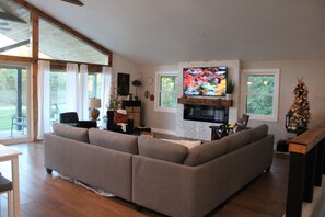 A modern living room with a sectional sofa, a flat-screen TV mounted above a fireplace, and a Christmas tree.