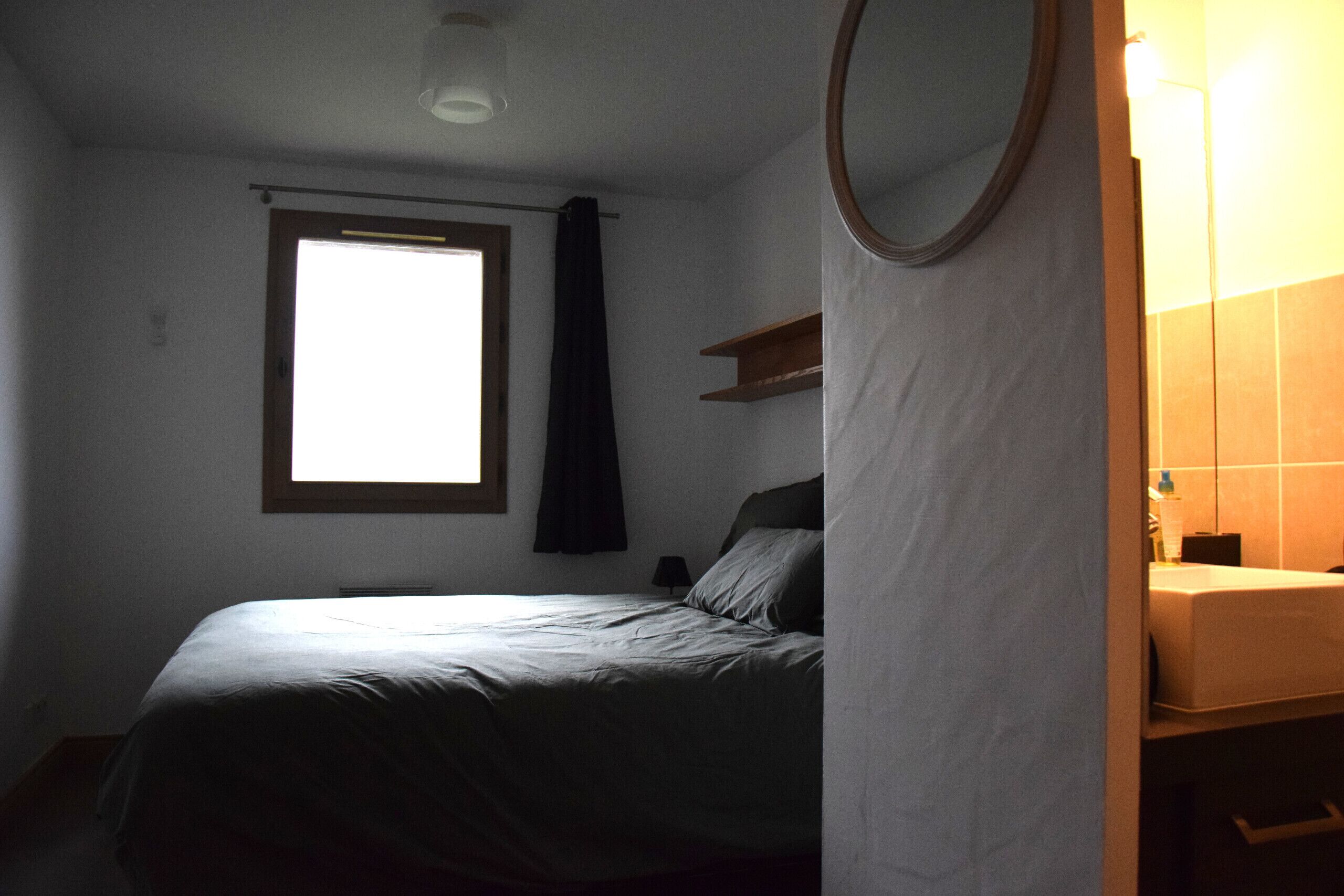 A bedroom with a bed, a window, a mirror, and a bathroom with a sink.
