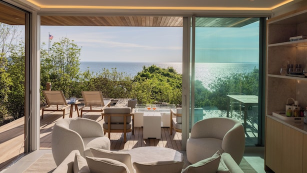 Un área de estar moderna al aire libre con vista al océano, que incluye sillones y una mesa.