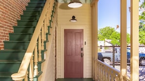 Un escalier avec des marches vertes et des balustrades beiges menant à une porte surmontée d’un luminaire.