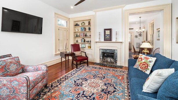 A living room with a fireplace, a television mounted on the wall, a ceiling fan, and a bookshelf. - 301 on Hancock - One Bedroom Apartment, Sleeps 4 (New Bern)