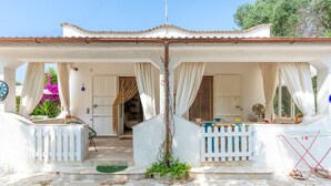 Ein Haus mit überdachter Veranda, einem weißen Zaun und einem kleinen Garten.