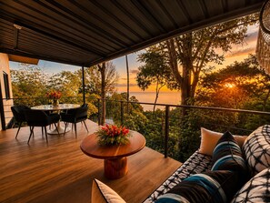 Un espace extérieur moderne, aménagé avec une table ronde en bois, des chaises noires et un canapé agrémenté de coussins à motifs.