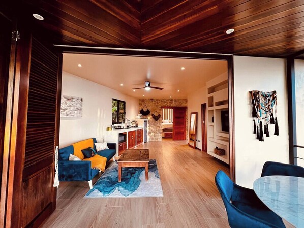 A spacious living area with a wooden ceiling, a blue sofa, a coffee table, and a stone wall in the background.