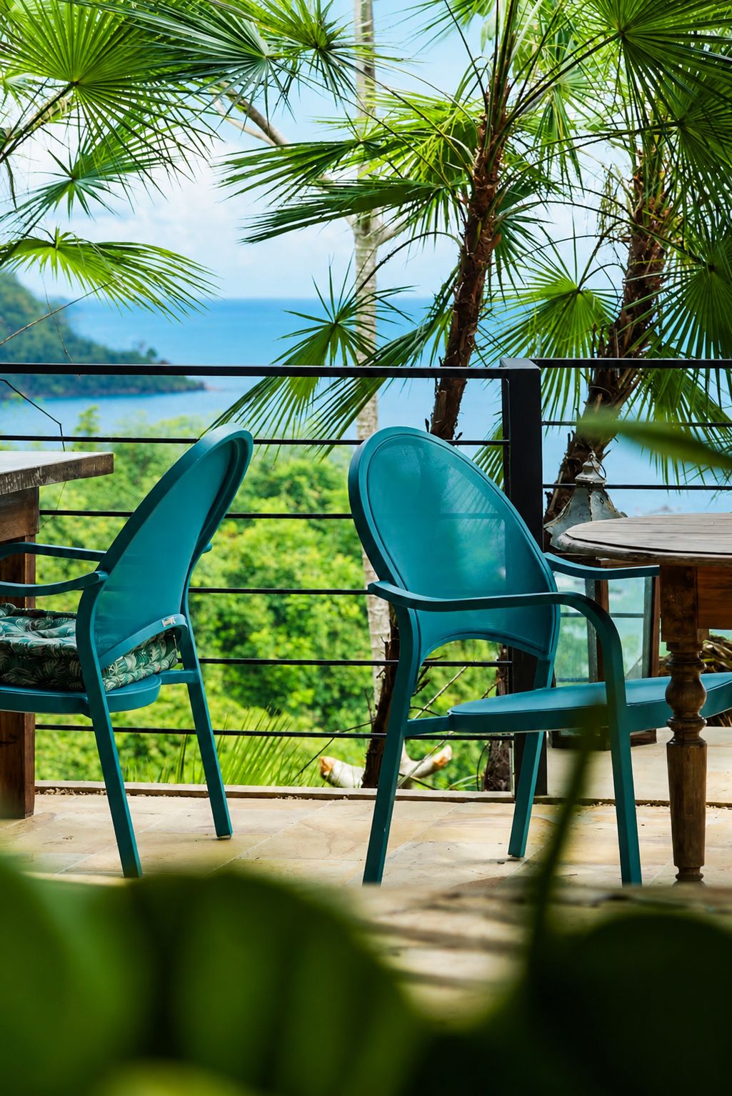 Dos sillas color turquesa con vista a un paisaje verde exuberante y al océano.