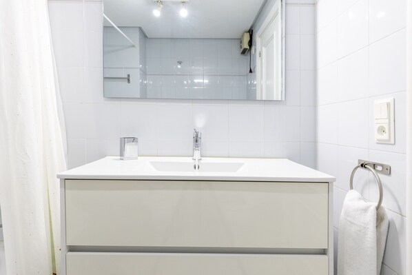 A modern bathroom with a white sink, mirror, and towel ring.