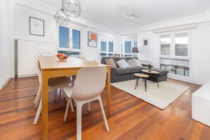 A modern living room with a wooden dining table, a grey sofa, and a small coffee table.