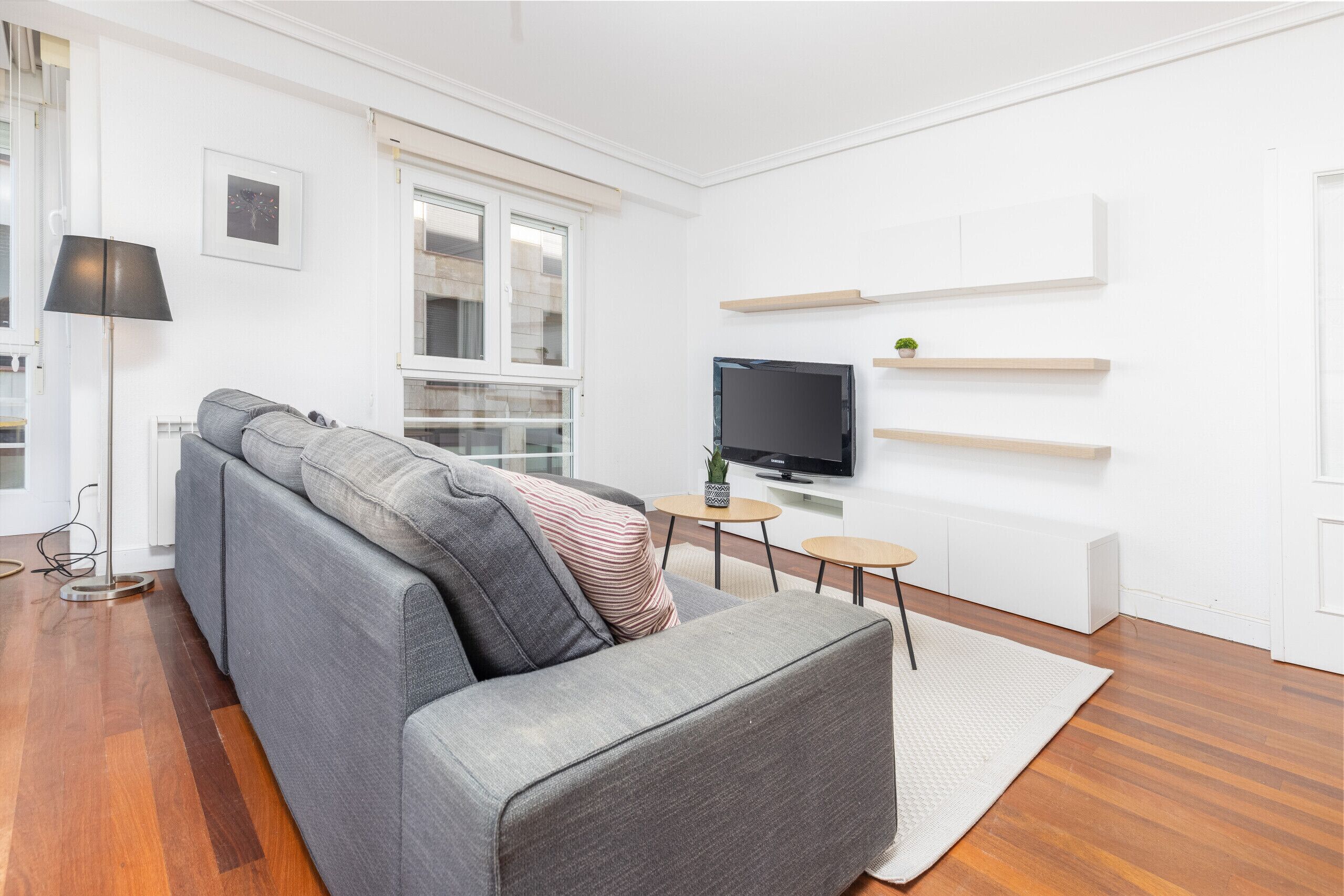 Een moderne woonkamer met een grijze bank, een flatscreen televisie en houten wandplanken.