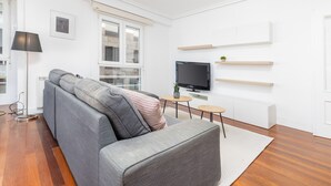 Een moderne woonkamer met een grijze bank, een flatscreen televisie en houten wandplanken.