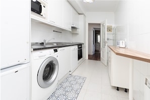 A compact kitchen with white cabinetry, a built-in washing machine, a microwave, and a wooden countertop.