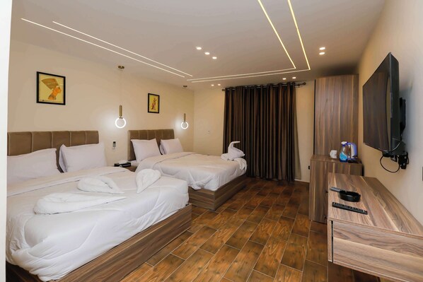 Two single beds with white bedding and headboards, a flat-screen TV, and a desk with a chair.