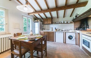 A rustic kitchen with wooden beams, a dining table with chairs, a washing machine, and a built-in oven. - Country House 'La Francesca' with Private Pool, Garden, and Wi-Fi (Cetona)