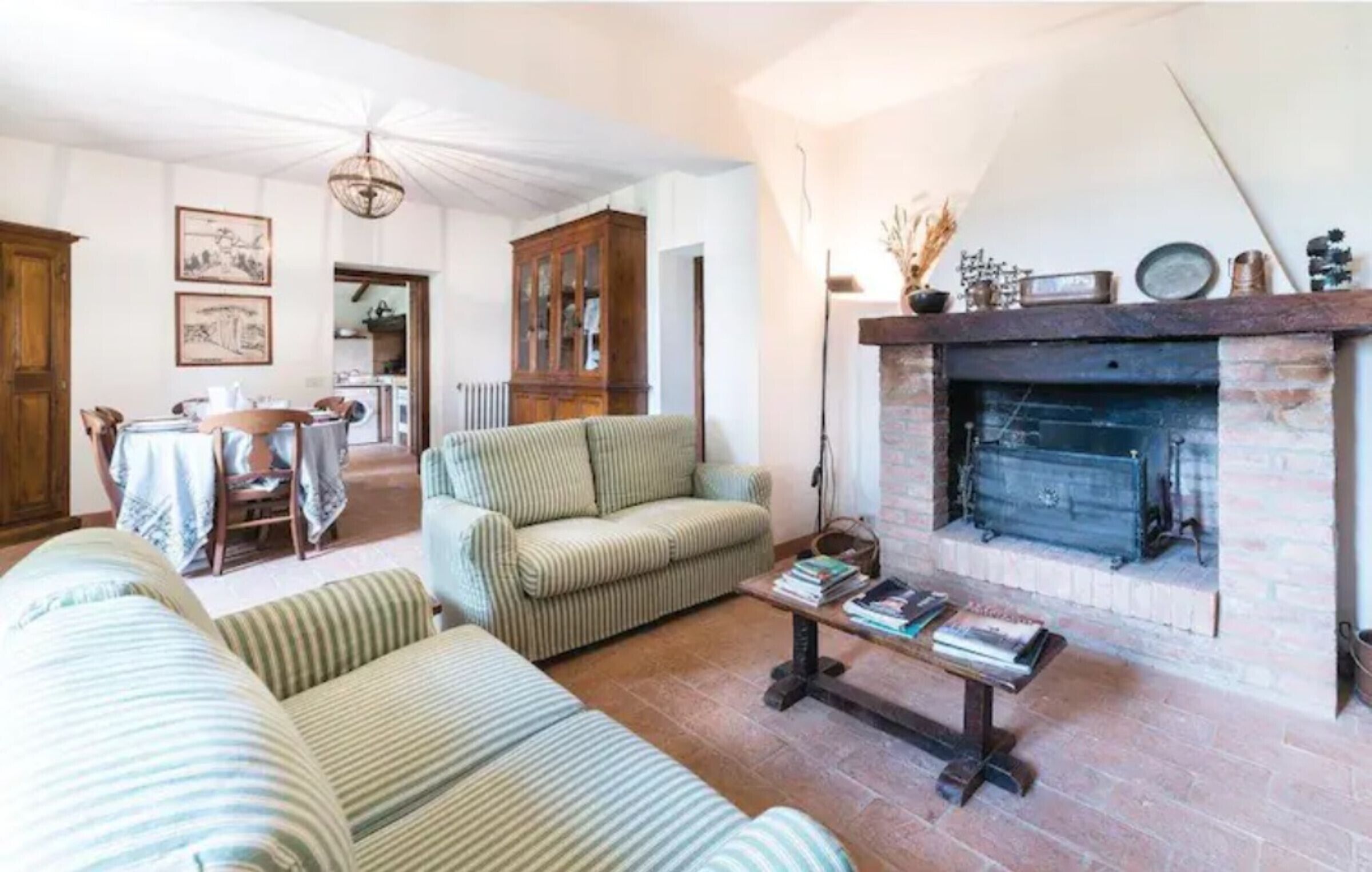 Una sala de estar con chimenea, sofás a rayas, una mesa de centro con libros y una zona de comedor con mesa y sillas.