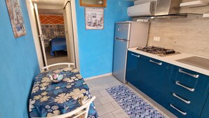 A compact kitchen with a gas stove, a refrigerator, and blue cabinets. - Apartment 'Balcone Sul Golfo' with Sea View, Wi-Fi and Air Conditioning (Alcamo)