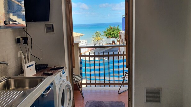 A kitchen with a washing machine, a sink, and a view of the sea through a balcony. - Apartment 'Balcone Sul Golfo' with Sea View, Wi-Fi and Air Conditioning (Alcamo)