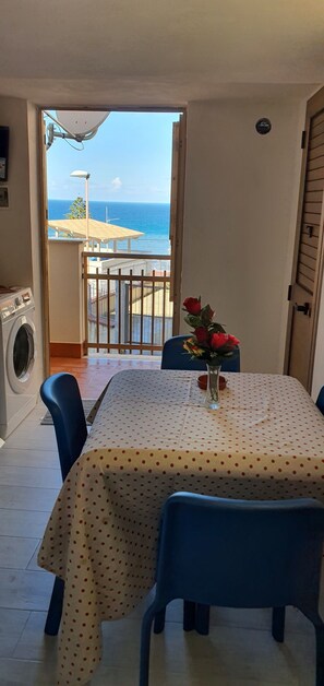 Ein Balkon mit Meerblick, ein Tisch mit bunt gepunktetem Tischläufer und eine Vase mit roten Blumen.