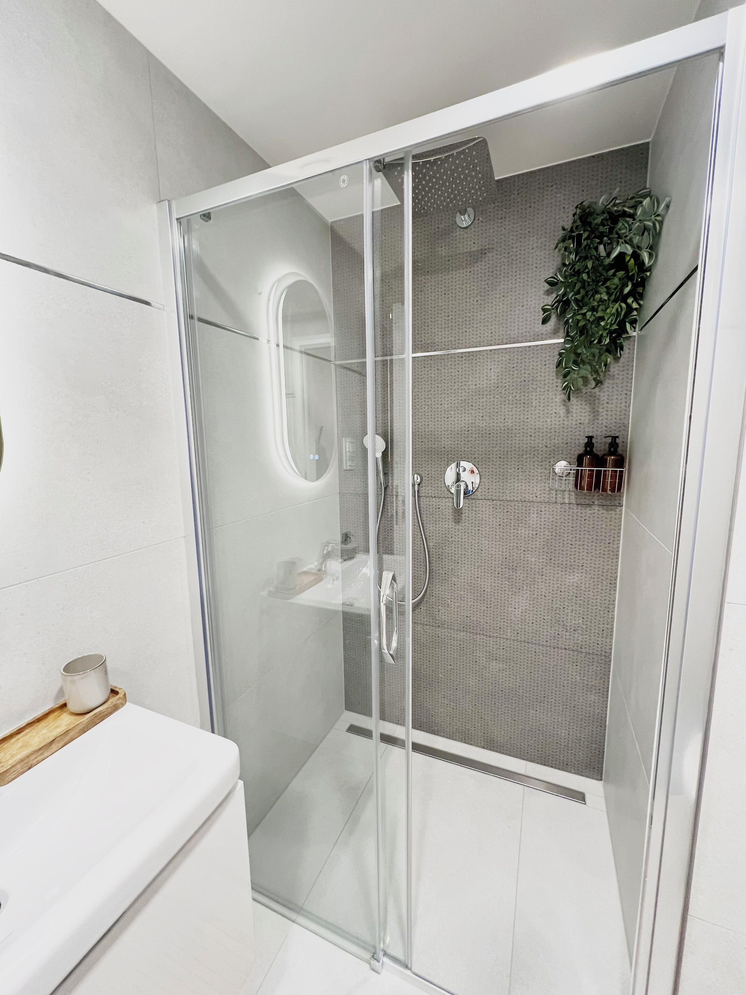 Un baño moderno con ducha de vidrio, un lavamanos blanco y una pequeña bandeja de madera.