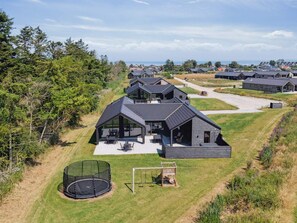 A modern residential complex with multiple houses featuring sloped roofs and large windows, surrounded by greenery and a clear sky. - 5 Star Holiday Home in Otterup (Otterup)