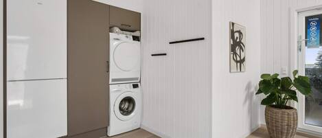 Un cuarto de lavandería con lavadora y secadora, una puerta con manija, y una planta en maceta.