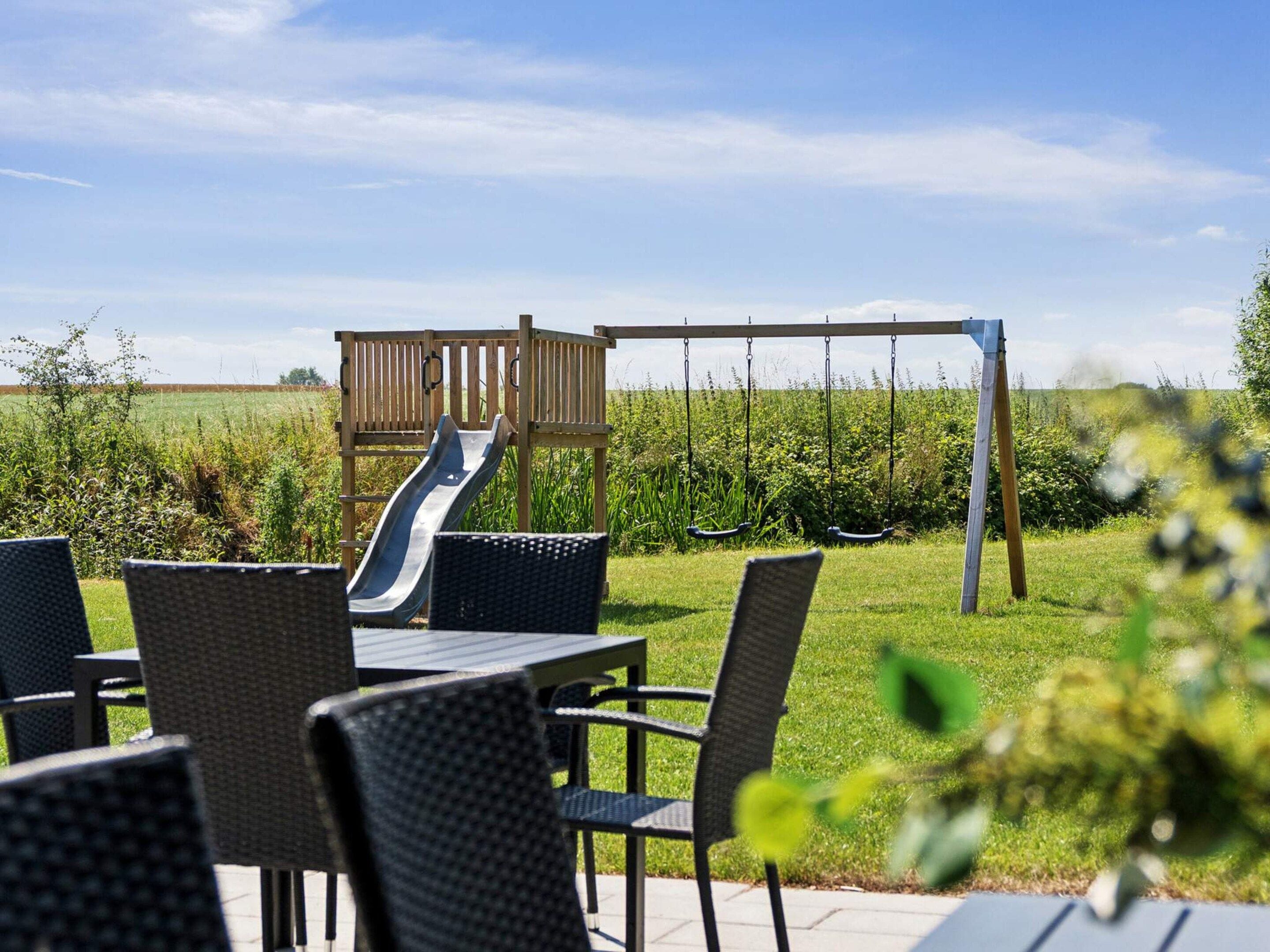An outdoor patio with wicker furniture, a wooden play structure with a slide, and a swing set.