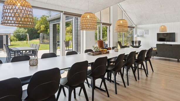 Un espace repas moderne avec une longue table, des chaises noires et trois suspensions en osier.