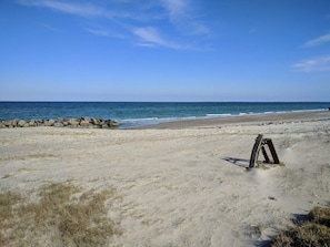 Una playa con una estructura de madera, un rompeolas rocoso y el océano al fondo.