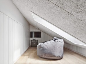 A modern loft bedroom with a sloped ceiling, a built-in TV, a small bedside table, and a bean bag chair. - 5 Star Holiday Home in Otterup (Otterup)