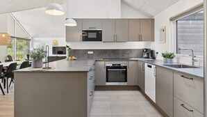 Une cuisine moderne dotée d’un îlot central, d’appareils électroménagers intégrés et d’une grande fenêtre qui laisse entrer la lumière naturelle.