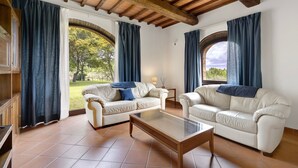 Un salon avec deux canapés, une table basse et une vue sur un jardin grâce à de grandes fenêtres.