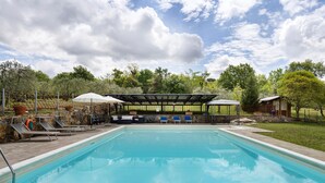 Une piscine entourée d’arbres et d’un mur de pierre, avec des chaises longues et des parasols.