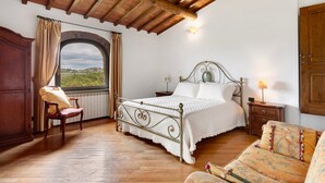 Une chambre à coucher avec un lit, une chaise, une table de chevet, une lampe et une vue par la fenêtre.
