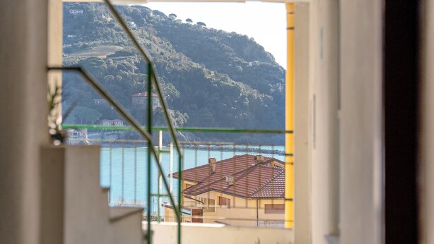 Vista a través de una ventana que muestra una casa, un cuerpo de agua y una colina al fondo.