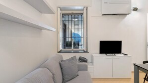 Una sala de estar moderna con un sofá, un televisor y una ventana con barrotes.