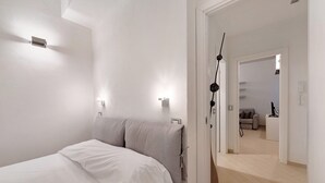 Un dormitorio con una cama, una puerta y un pasillo que da a una sala de estar.