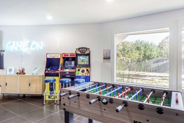 A room with a foosball table, arcade games, and a neon sign that reads "GAME ON".