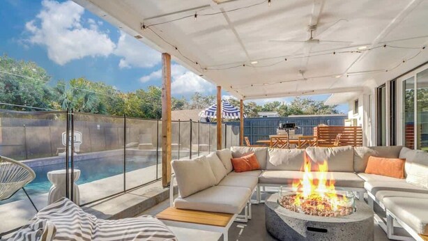 A modern outdoor living area with a fire pit, seating, and a pool. - Heated Pool + Outdoor Theater | Sleeps 16 w/ Games (San Antonio)