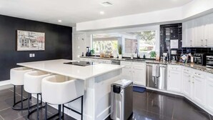 A modern kitchen with white cabinetry, a large island with bar stools, stainless steel appliances, and a black backsplash. - Heated Pool + Outdoor Theater | Sleeps 16 w/ Games (San Antonio)