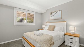 A bedroom with a bed, bedside tables, a window with blinds, and a painting on the wall.