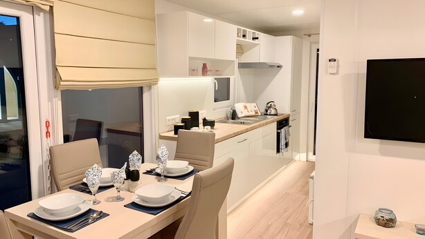 A modern kitchen with white cabinets, a dining area with a table set for four, and a small island with a sink. - Holiday Home 'Domaine 3016' with Shared Pool, Wi-Fi and Air Conditioning (Roquebrune-sur-Argens)