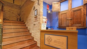 A hotel reception desk with a wooden counter, a sign indicating room availability, and a staircase with wooden steps.